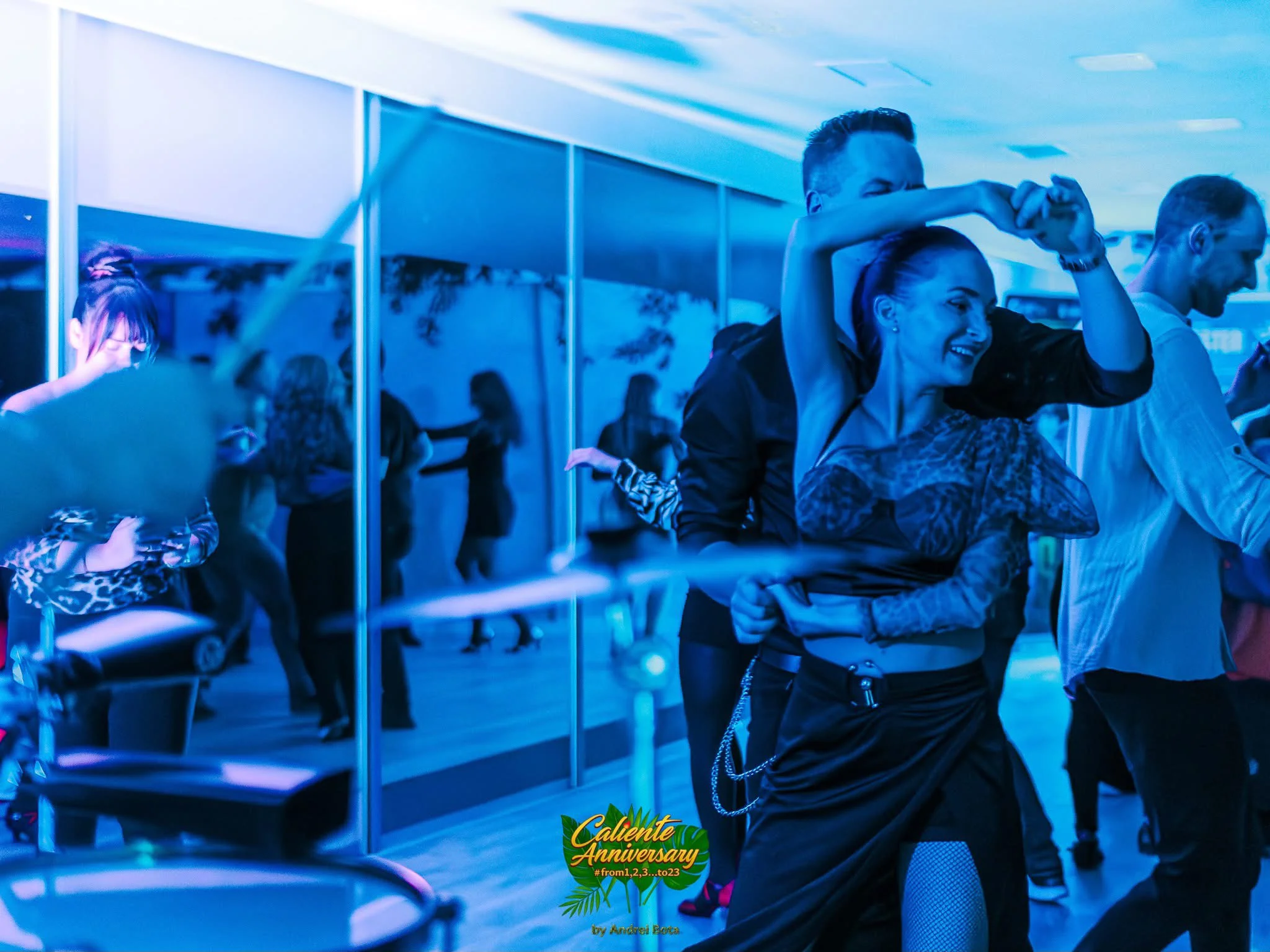 Oameni dansează energic într-o sală modernă de dans latino din Cluj, iluminată albastru